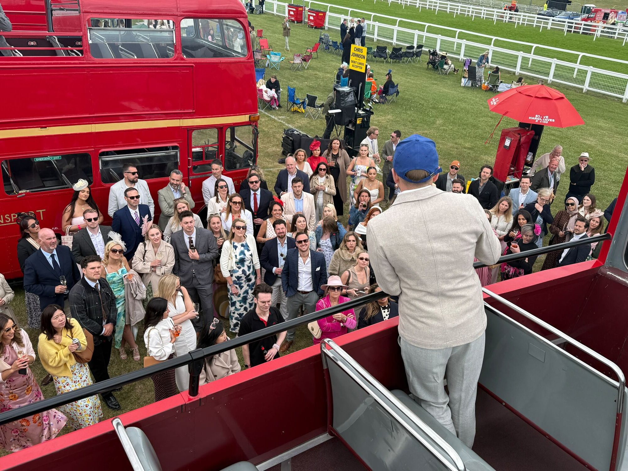 Guests at a Novello event at Epsom racecourse, listening to a speaker on an open-top bus
